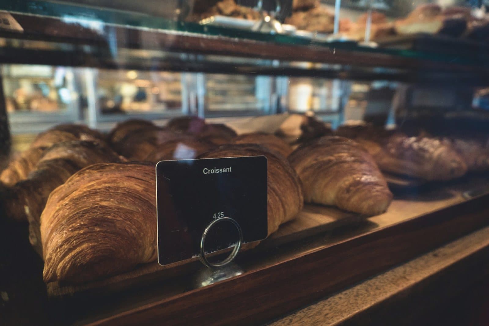 Croissants on a café counter behind glass, with a price card