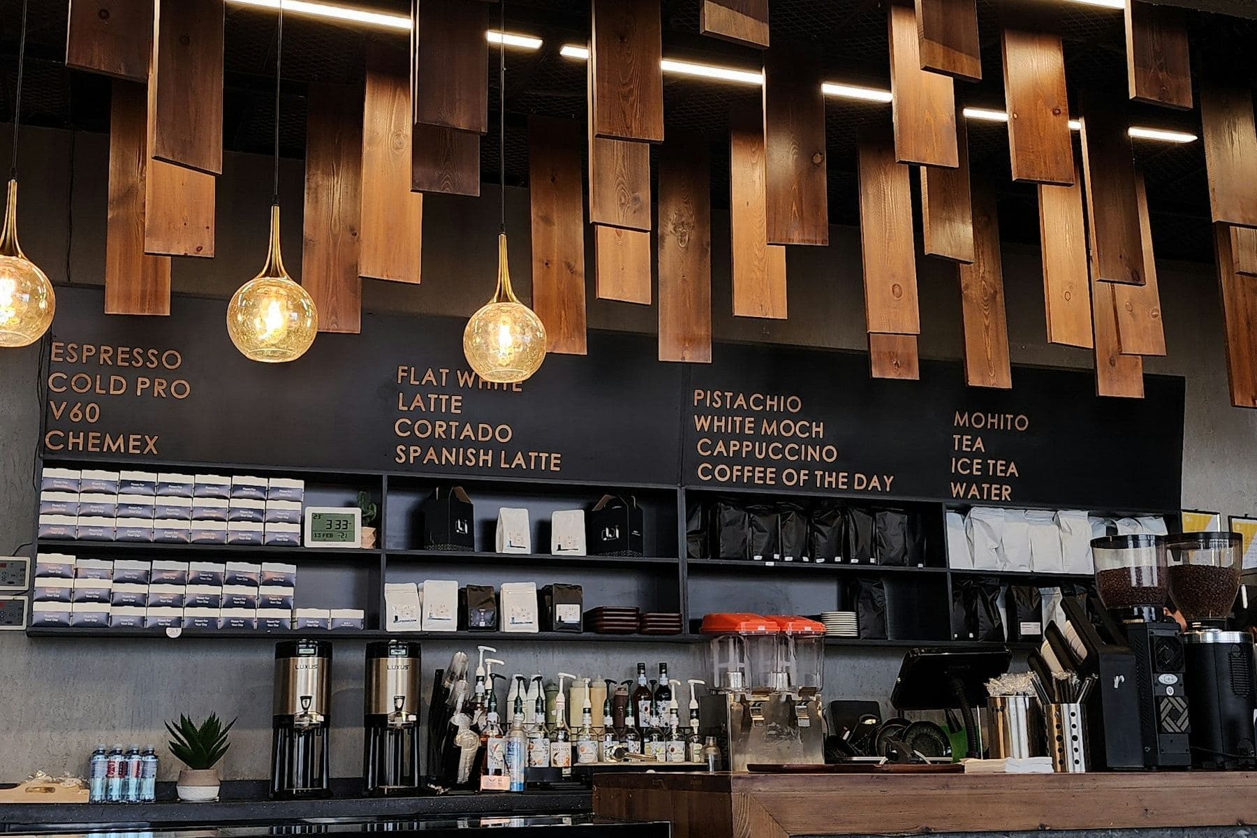 A café counter in Jeddah: a menu board of coffees above shelves of beans, under hanging timber and glass lamps